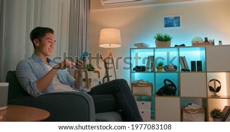 asian young man using smart home app to control light colors in the evening at home Royalty-Free Stock Photo #1977083108