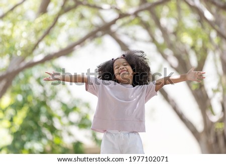 A little  curly hair girl arms outstretched under the tree.	 Royalty-Free Stock Photo #1977102071