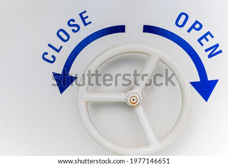 Iron wheel door handle with direction for close or open on navy white wall. Iron door handle in round shape on a yacht or sailing boat