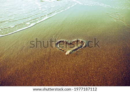 Heart drawn on a sand near sea comb line (green and violet toning)