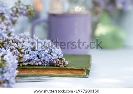 Spring time. The concept of "Good morning". A fancy violet coffee mug, an old book, a straw hat, and purple lilac. Beautiful still life.