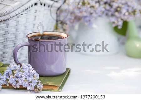 Spring time. The concept of "Good morning". A fancy violet coffee mug, an old book, a straw hat, and purple lilac. Beautiful still life.