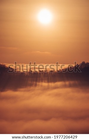 Glowing orange ball illuminates floating clouds around the mountains in spring time. Walking above the clouds at sunset. Orange tone of the whole image.