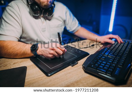 Designer works at home at night on a graphics tablet at work. Male artist draws on a tablet, close-up photo of hands at work.