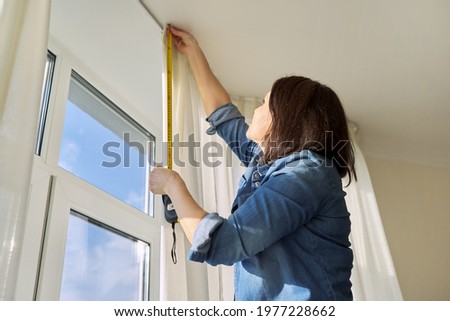 Service for sewing and hanging curtains. Woman with tape measure measuring window Royalty-Free Stock Photo #1977228662