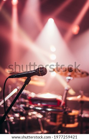 Microphone on a stage with a drum set and pink lights in the background on a concert