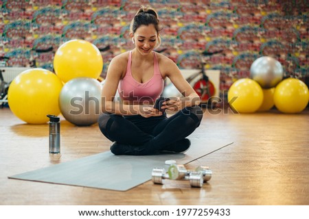 Young attractive woman using a smartphone while training in the gym
