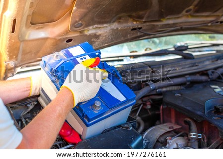 Maintenance of the machine. A male car mechanic takes out a battery from under the hood of a auto to repair, charge or replace it. Royalty-Free Stock Photo #1977276161