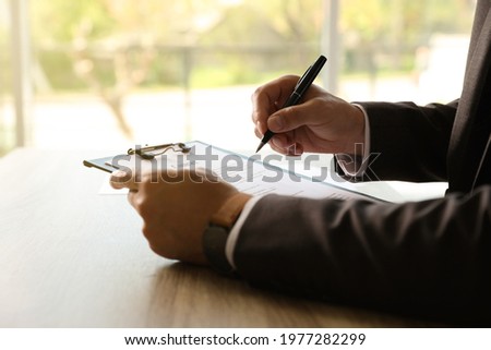 Businessman signing document at table indoors, closeup