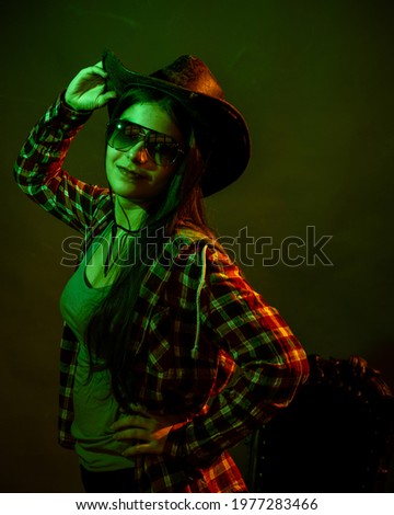 A girl in a plaid shirt with a cowboy hat illuminated by multicolored light