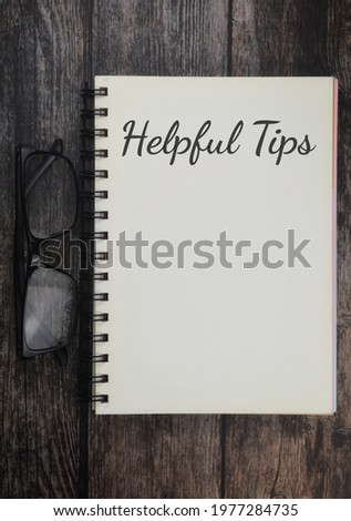 Top view of book and spectacles with Helpful Tips wording over a wooden background. Selective focus image. 