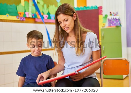 Educator or childminder with child reading a book in kindergarten or after-school care center
