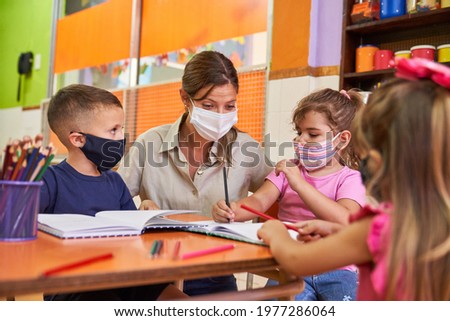 Children and educator in daycare with face mask because of Covid-19 and coronavirus Royalty-Free Stock Photo #1977286064