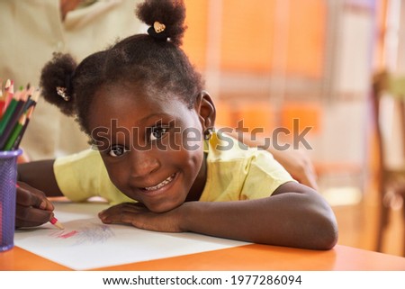 Happy girl with pigtails paints a colorful picture with crayons in the elementary school painting class Royalty-Free Stock Photo #1977286094