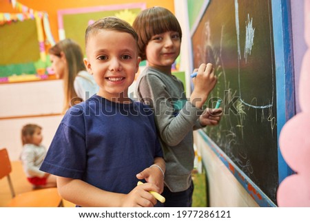 Children paint with chalk on the blackboard in preschool or elementary school in creative painting class Royalty-Free Stock Photo #1977286121