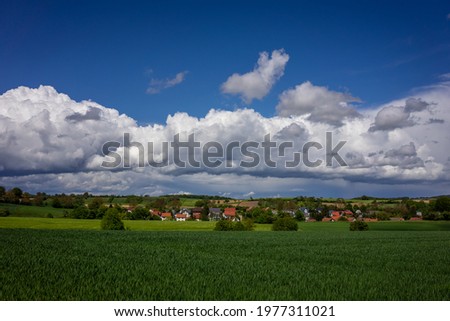 Beautiful green spring landscape in Kraichgau, Germany with village and cloudy sky in background.