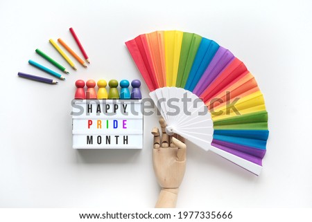 LGBTQ pride month decor. Text Happy Pride Month on lightbox. Rainbow pattern objects on off white background. Wood hand model hold rainbow fan. Wooden pencils and figurines. Celebrate diversity.