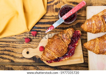 croissants with raspberries and raspberry jam on a wooden table. rustic top view
