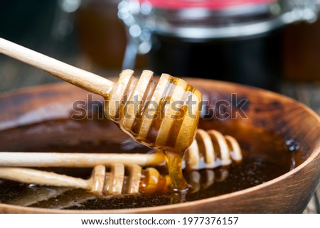 a spoon for honey together with high-quality bee honey, an old table on which there is a healthy and sweet bee honey and a homemade wooden spoon that allows you to transfer and pour honey