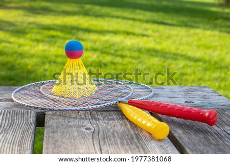 Badminton game rackets and shuttlecock on wooden table with green grass backgroud in the park on a sunny summer day. Active lifestyle concept. Fun outdoors leisure activities for a family.