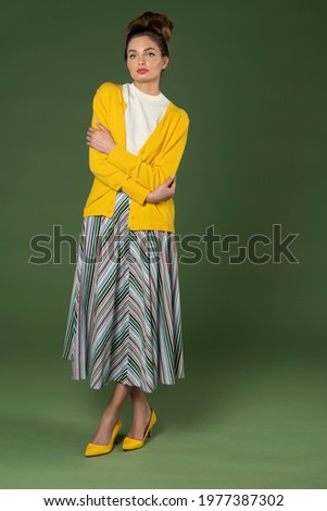 young and beautiful model , with perfect hair style , with old fashion outfit , colorful striped gown and yellow jacket , on green background