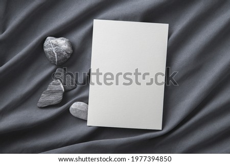 Blank greeting card or postcard mockup on grey cloth and natural stones..