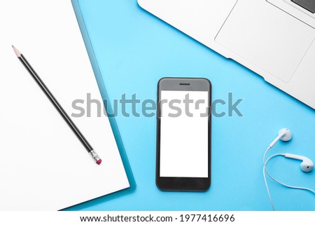 Modern mobile phone with laptop, earphones and clipboard on color background