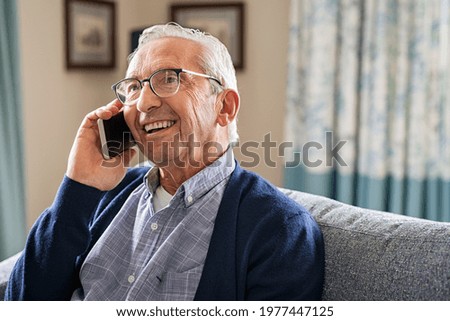 Smiling old man talking over smartphone while relaxing at home. Senior man after retirement using smart phone to connect with friends and family. Carefree elder talking over phone with her daughter. Royalty-Free Stock Photo #1977447125