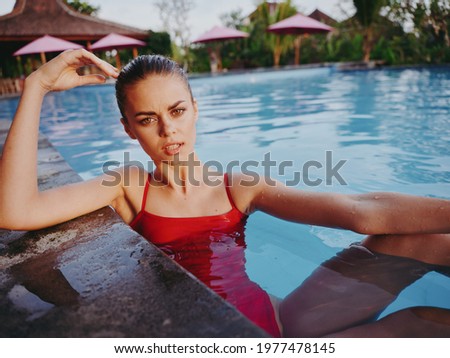 woman in red swimsuit swim in the pool in summer and sun loungers in the background