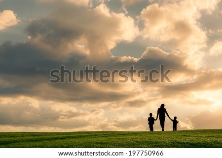 Family silhouette against a bright cloudy sky at sunset. Mother and two boys walking holding hands
