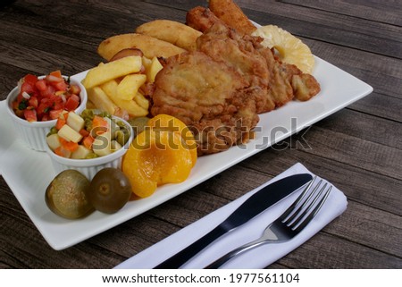 Traditional Cuban filet. Made with Breaded Steak, Banana, Breaded Cheese and Ham. French Fries with Bacon. Vinaigrette, vegetables, and fruits. Served on the porcelain platter. Cutlery on napkin.