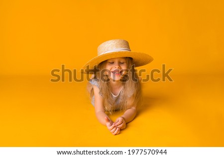 laughing little blonde girl in a straw hat lies on a yellow background with space for text. Summer background