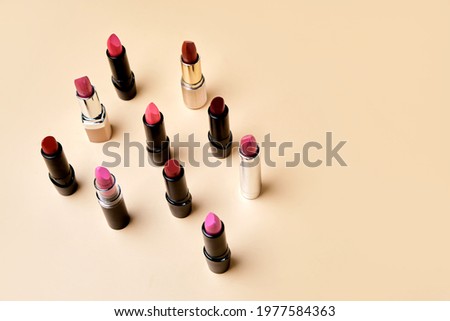 Flat lay composition with Set of different shapes and colors of lipsticks are scattered with space for text on beige background