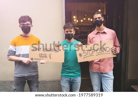 Three friends with masks display two signs with the message stop covid, just vaccinated.To underline the concept the friends score 1 covid 0.Concept of friendship,new normal,fight against the pandemic