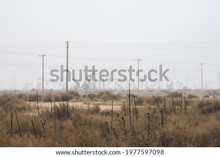 Distant oil pump jacks pumping crude oil in a foggy field