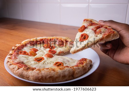 Slice of pizza raised by one hand. Gastronomic picture