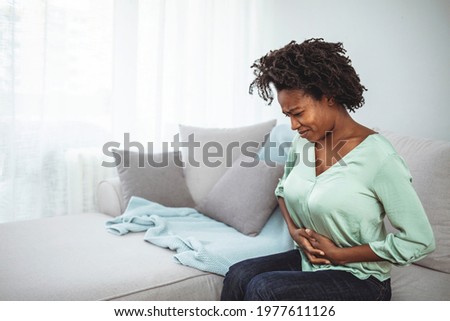 Closeup shot of a woman suffering with stomach cramps at home. Abdominal pain patient woman having medical exam with doctor on illness from stomach cancer, irritable bowel syndrome Royalty-Free Stock Photo #1977611126