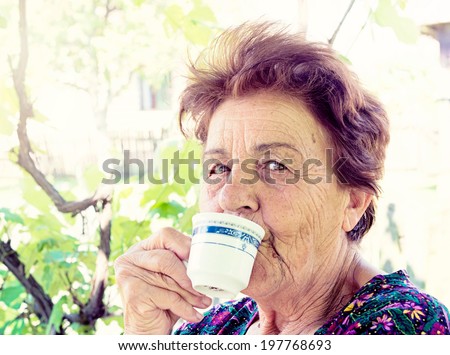 Old woman drink coffee and smile in backyard