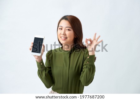 Beautiful smiling girl confident holding mobile phone blank screen and showing OK gesture