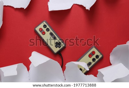 Retro gamepads and white torn paper sheets on red background. Minimalistic background. Top view.
