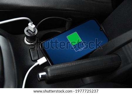 Mobile phone ,smartphone, cellphone is charged ,charge battery with usb charger in the inside of car. modern black car interior. Royalty-Free Stock Photo #1977725237