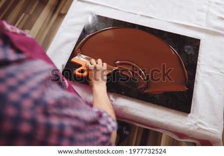 Top view of chocolatier holding cake scraber and cooling melted chocolate mass on a marble table. Closeup Royalty-Free Stock Photo #1977732524