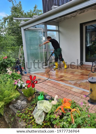 Man cleaning conservatory with a pressure washer - high pressure washer on patio glass surface