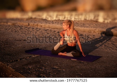 Young blonde woman in sportswear performs yoga asanas, exercises on the seashore at sunrise. The girl goes in for sports, works out breathing, meditates, performs Dove pose. Healthy mind in a fit body Royalty-Free Stock Photo #1977767525