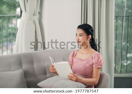 Beautiful young woman reading magazine and lying on sofa at home