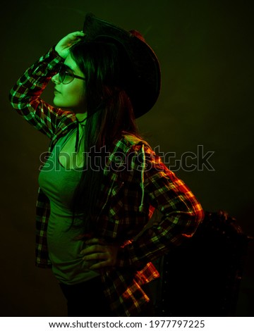 A girl in a plaid shirt with a cowboy hat illuminated by multicolored light