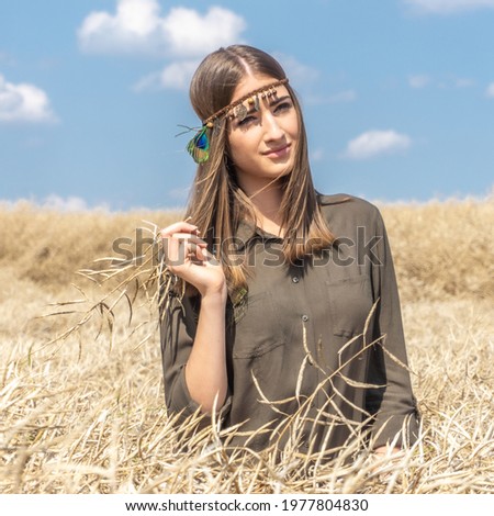 Beautiful scenery in the rural agricultural field of the natural environment with a single girl sitting in the deep yellow dry grass in her stylish summer clothes. Fashion and beauty photography.