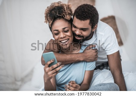 Man hugging woman sitting with smartphone
