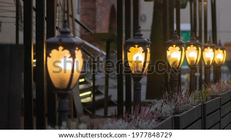 Small, electric street lanterns glowing in the dark by the outdoor terrace of a restaurant. Focus on the second lantern.