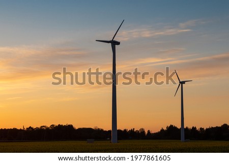 landscape photography with orange sunset sky and two wind turbines in yellow raps field 